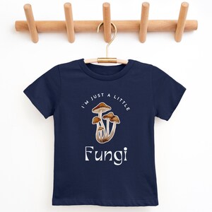 May include: A navy blue t-shirt with a white graphic of mushrooms and the text "I'm just a little Fungi".