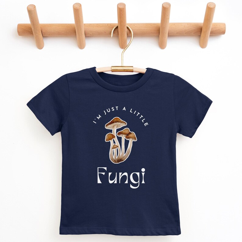 May include: A navy blue t-shirt with a white graphic of mushrooms and the text "I'm just a little Fungi".