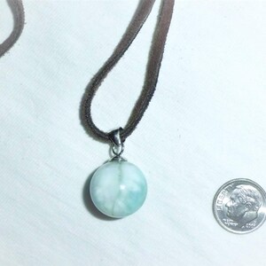 May include: A light blue and white round pendant necklace with a silver bail and a brown suede cord.