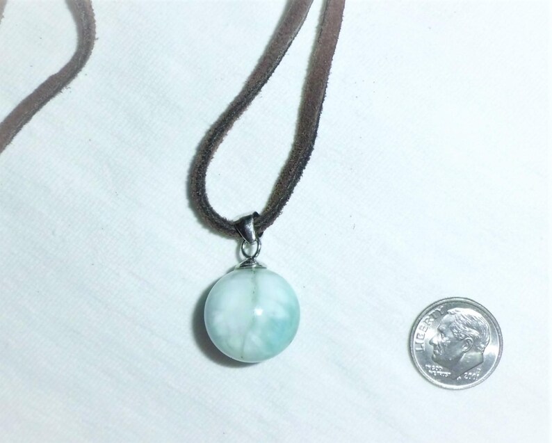 May include: A light blue and white round pendant necklace with a silver bail and a brown suede cord.