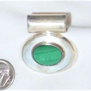 May include: A silver pendant with an oval, bright green stone set in a silver bezel. The pendant has a rectangular bail at the top. A U.S. dime is next to the pendant for size comparison.