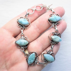 May include: A silver bracelet with five oval-shaped blue gemstone charms. The bracelet has a lobster claw clasp.