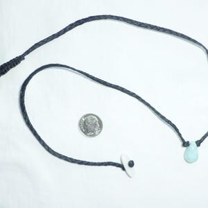 K&ouml;nnte beinhalten: Eine schwarze Schnurkette mit einem hellblauen tropfenf&ouml;rmigen Anh&auml;nger und einem wei&szlig;en und schwarzen Augenanh&auml;nger.