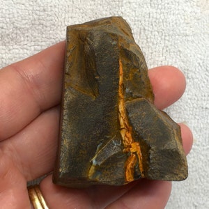 Puede incluir: Una roca áspera de color marrón oscuro con una fina veta de ópalo naranja y blanco que la atraviesa.