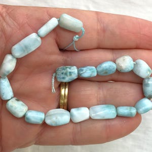 Könnte beinhalten: Eine Kette aus hellblauen und weißen Edelsteinperlen. Die Perlen sind glatt und oval geformt. Die Perlen sind auf einer dünnen weißen Schnur aufgefädelt.