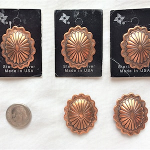 Peut inclure: Cinq boutons conchos de couleur cuivre avec un motif en forme de soleil. Les boutons sont sur des cartes noires avec le texte "Sterling Silver Made in USA".