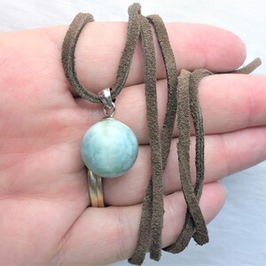 May include: A light blue round gemstone pendant on a brown suede cord necklace.