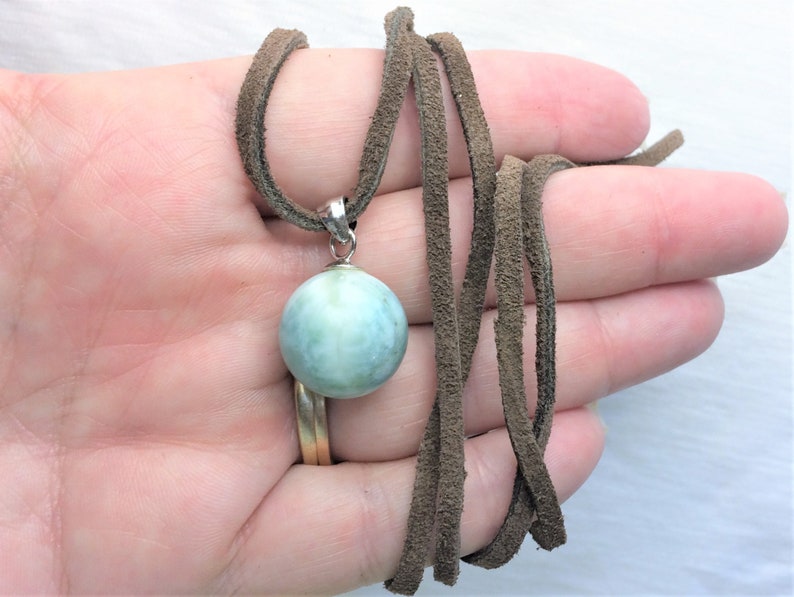 May include: A light blue round gemstone pendant on a brown suede cord necklace.