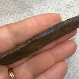 May include: A long, thin piece of brown and blue opal with a rough, natural texture.