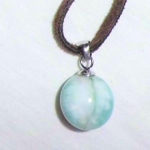 May include: A light blue and white round pendant with a silver bail hangs from a brown suede cord.