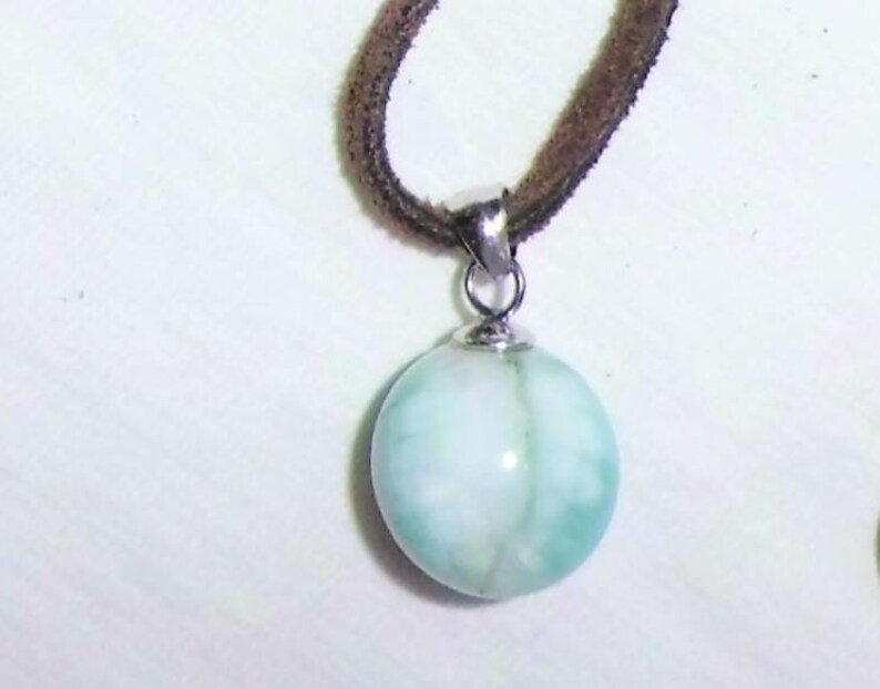 May include: A light blue and white round pendant with a silver bail hangs from a brown suede cord.