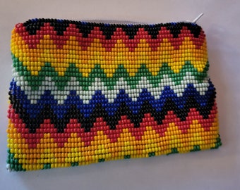 May include: A small beaded pouch with a zipper closure. The pouch is made with colorful beads in a zig-zag pattern, including red, orange, yellow, green, blue, white, and black.