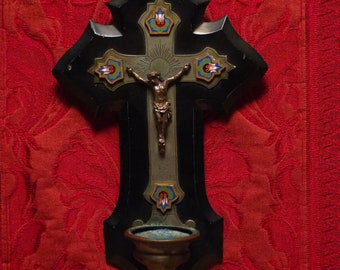 May include: A black wooden crucifix with a metal Jesus figure and decorative floral accents. The crucifix has a small cup at the bottom.