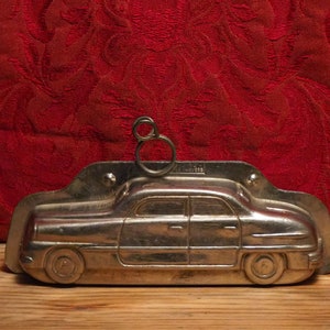 May include: A silver metal mold shaped like a vintage car. The mold has a loop on top for hanging.
