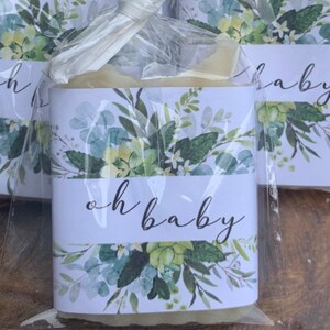 May include: A white bar of soap wrapped in clear cellophane with a white label featuring a watercolor floral design and the text "oh baby".