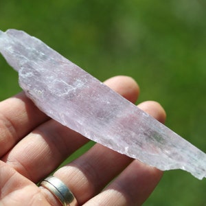 May include: A translucent, pale pink selenite crystal with a striated surface. The crystal is long and thin, with a slightly pointed end.