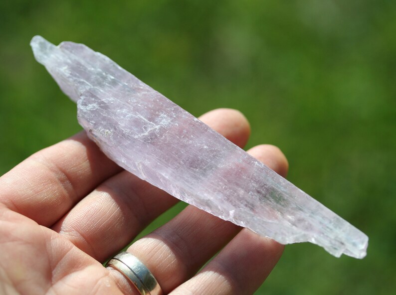 May include: A translucent, pale pink selenite crystal with a striated surface. The crystal is long and thin, with a slightly pointed end.