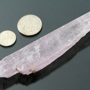 May include: A pale pink selenite crystal, about 5 inches long, next to two US quarters for scale.