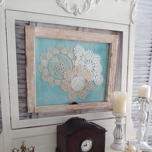 May include: A white painted wooden cabinet with a framed picture of three white doilies on a blue background. The cabinet has a small wooden clock on top and a gold crown on the bottom. The text "RIGHT UP MY ALLEY DESIGNS" is written on the surface of the cabinet.