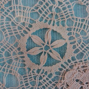 May include: A close-up of a white crocheted doily with a delicate floral design. The doily is laid on a blue mesh background.