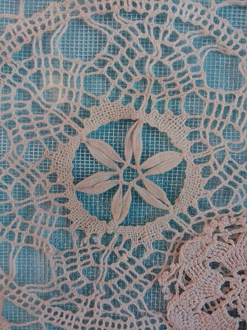 May include: A close-up of a white crocheted doily with a delicate floral design. The doily is laid on a blue mesh background.