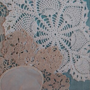 May include: A collection of white and cream crocheted doilies with intricate floral patterns. The doilies are arranged on a blue background.