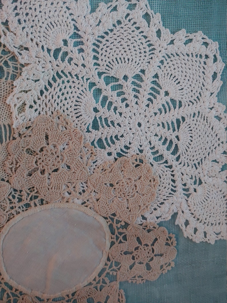 May include: A collection of white and cream crocheted doilies with intricate floral patterns. The doilies are arranged on a blue background.