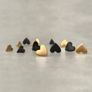 May include: A set of small heart-shaped earrings in gold and black. The earrings are made of metal and have a simple, minimalist design.