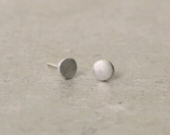 May include: A pair of silver stud earrings with a circular design. The earrings have a brushed finish.