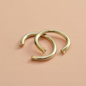 May include: Two gold-colored metal bangles, each with a rounded, slightly curved shape. The bangles are stacked on top of each other.