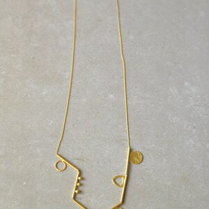 May include: A gold necklace with a geometric design featuring multiple circles, a triangle, and a bar. The necklace is made of a thin chain and has a delicate, minimalist style.