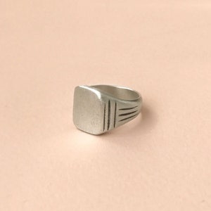 May include: A silver signet ring with a square face and a simple engraved design.