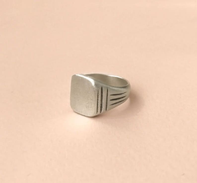 May include: A silver signet ring with a square face and a simple engraved design.