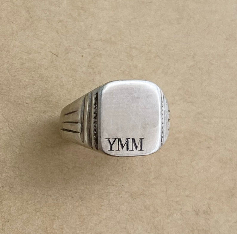 May include: A silver signet ring with a square face and the initials "YMM" engraved on it.