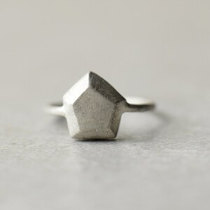 May include: A silver ring with a geometric, faceted, diamond-shaped stone.