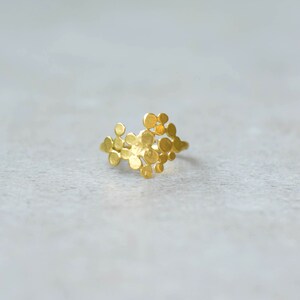 May include: A gold ring with a unique design featuring a cluster of small, round, textured shapes.