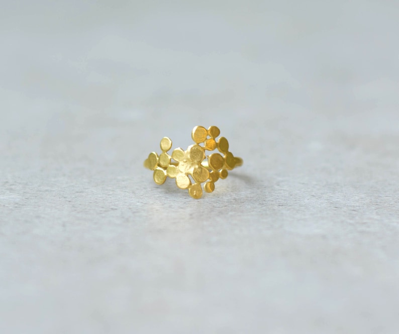 May include: A gold ring with a unique design featuring a cluster of small, round, textured shapes.