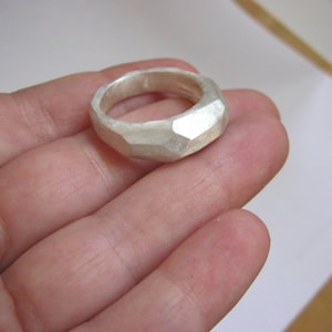 Könnte beinhalten: Ein silberner Ring mit einem strukturierten, facettierten Design. Der Ring ist breit und hat eine abgerundete Form.
