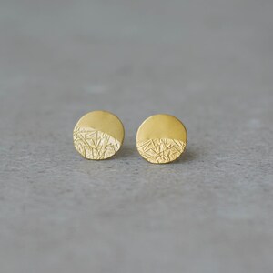 May include: A pair of gold-toned stud earrings with a textured, circular design. The earrings have a textured, organic pattern on one half of the circle.