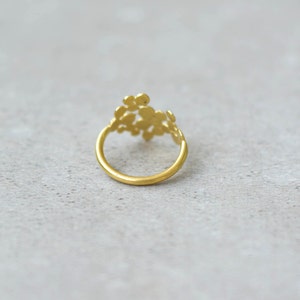 May include: A gold ring with a delicate, floral design. The ring is made of a single band with a cluster of small, round shapes that resemble flowers.
