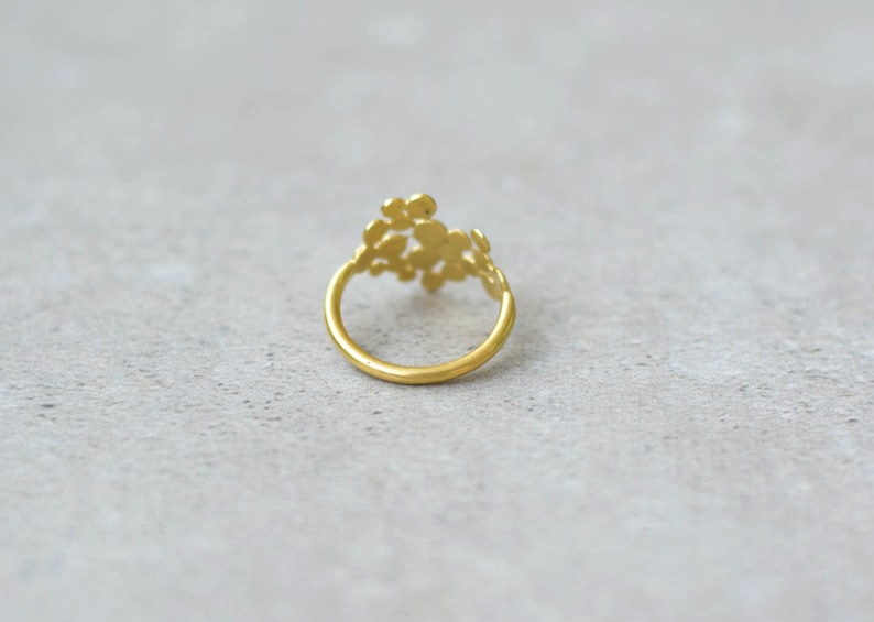 May include: A gold ring with a delicate, floral design. The ring is made of a single band with a cluster of small, round shapes that resemble flowers.