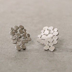 Peut inclure: Une paire de boucles d'oreilles en argent avec un design unique et abstrait. Les boucles d'oreilles sont composées de petites formes rondes qui sont regroupées pour créer un aspect texturé et organique.