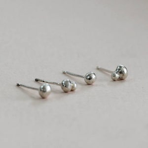 May include: Three pairs of silver stud earrings. Two pairs feature a single round bead, while the third pair has two round beads.