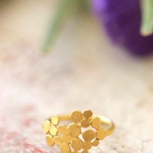 May include: A gold ring with a unique design featuring a cluster of small, round, textured shapes.