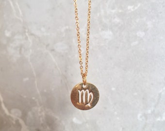 May include: A gold chain necklace with a small, round pendant featuring a cut-out Virgo zodiac sign.