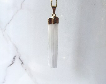 May include: A gold chain necklace with a white selenite crystal pendant. The crystal is a long, thin, rectangular shape with a smooth, polished surface.