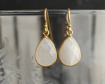 May include: A pair of gold dangle earrings with white teardrop-shaped stones.