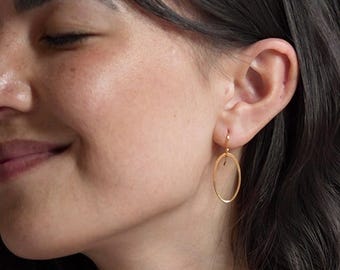 May include: A gold-toned earring featuring a thin, circular hoop design suspended from a simple hook wire. The earring is crafted from a slender metallic wire formed into an open circle, providing a delicate and lightweight appearance on the ear.