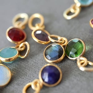 Può includere: Primo piano di diversi gioielli color oro con pietre preziose colorate. Le pietre preziose sono di vari colori, tra cui rosso, blu, verde e giallo. Ogni pietra preziosa è incastonata in una lunetta dorata e collegata con un piccolo anello d'oro.