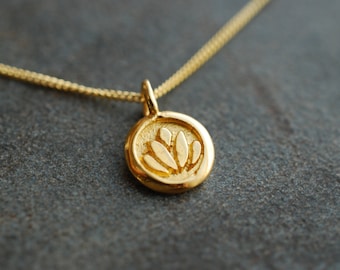 May include: A gold necklace with a small round pendant featuring a raised lotus flower design.